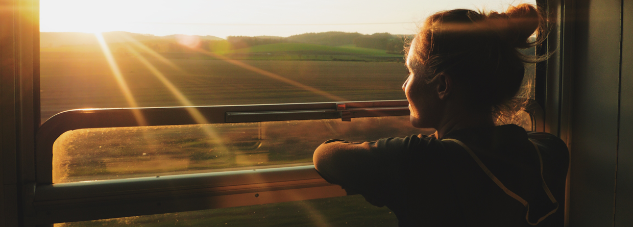Slow travel; vrouw geniet vanuit een trein van het landschap en de zon