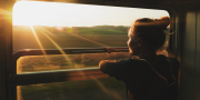 Slow travel; vrouw geniet vanuit een trein van het landschap en de zon