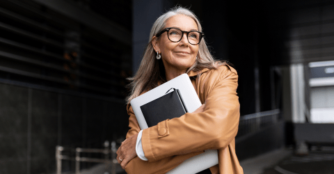 Een dame met bril staat buiten kantoor met een laptop in haar handen