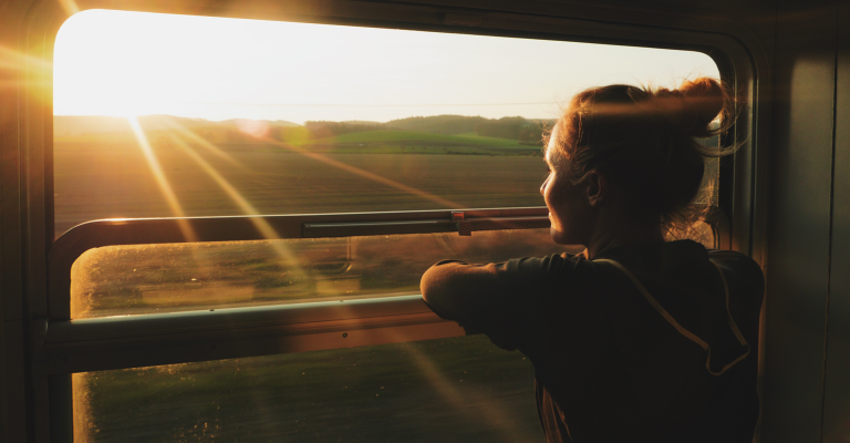 Slow travel; vrouw geniet vanuit een trein van het landschap en de zon